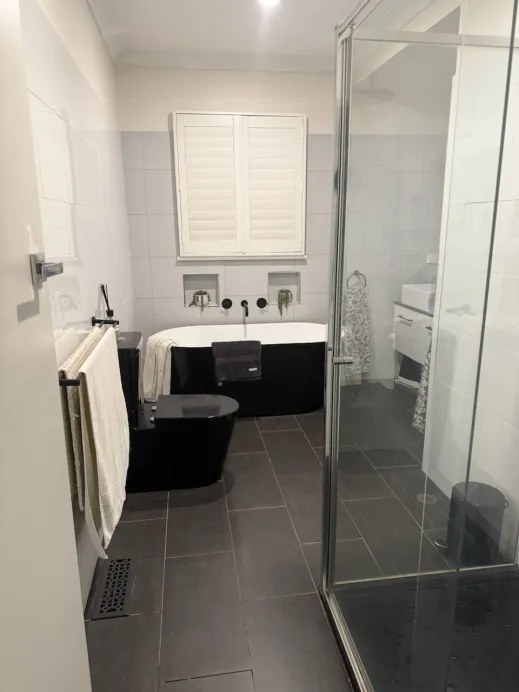 Original Newcomb bathroom before renovation, with a black bath, dark floor tiles and partial-height wall tiling