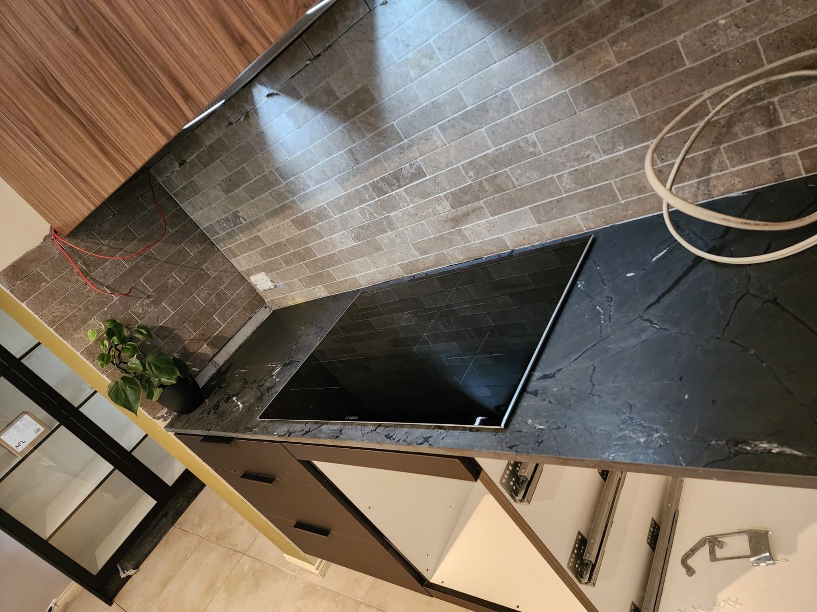 Textured brick-look splashback tile beside the dark stone benchtop and induction cooktop